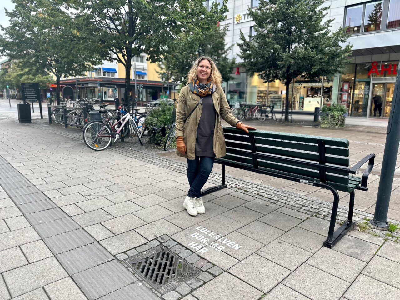 Människa på gångstråk vid parkbänk och text vid brunn "Luleälven börjar här"