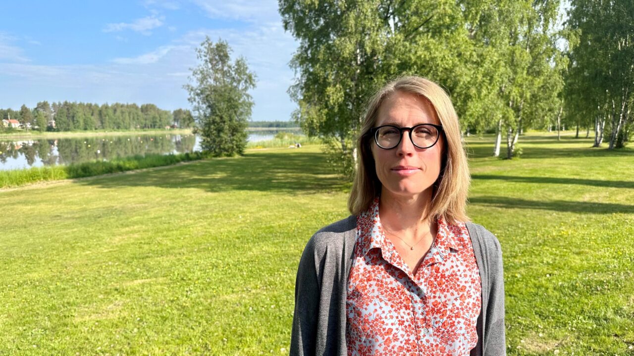 Bild på människa på en stor gräsplätt, med träd mot blå himmel och med vatten i bakgrunden