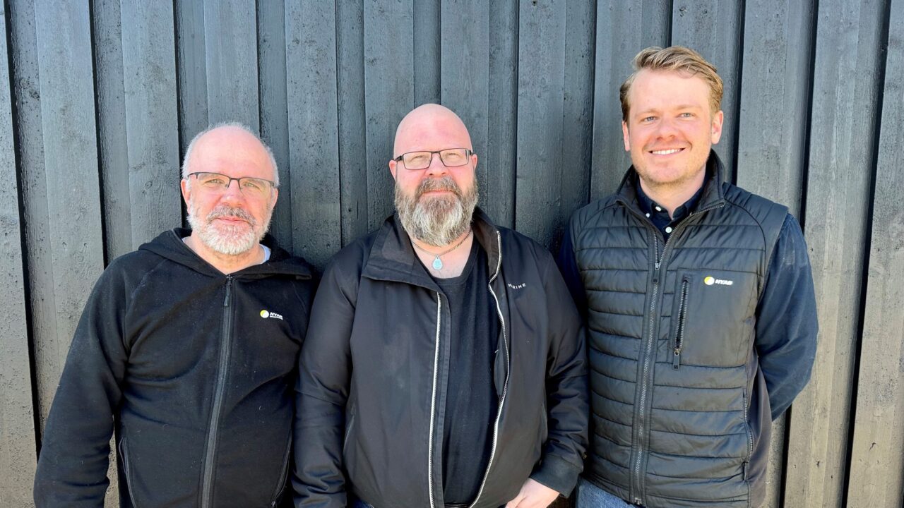 Tre personer i svarta kläder mot en svart husvägg utomhus