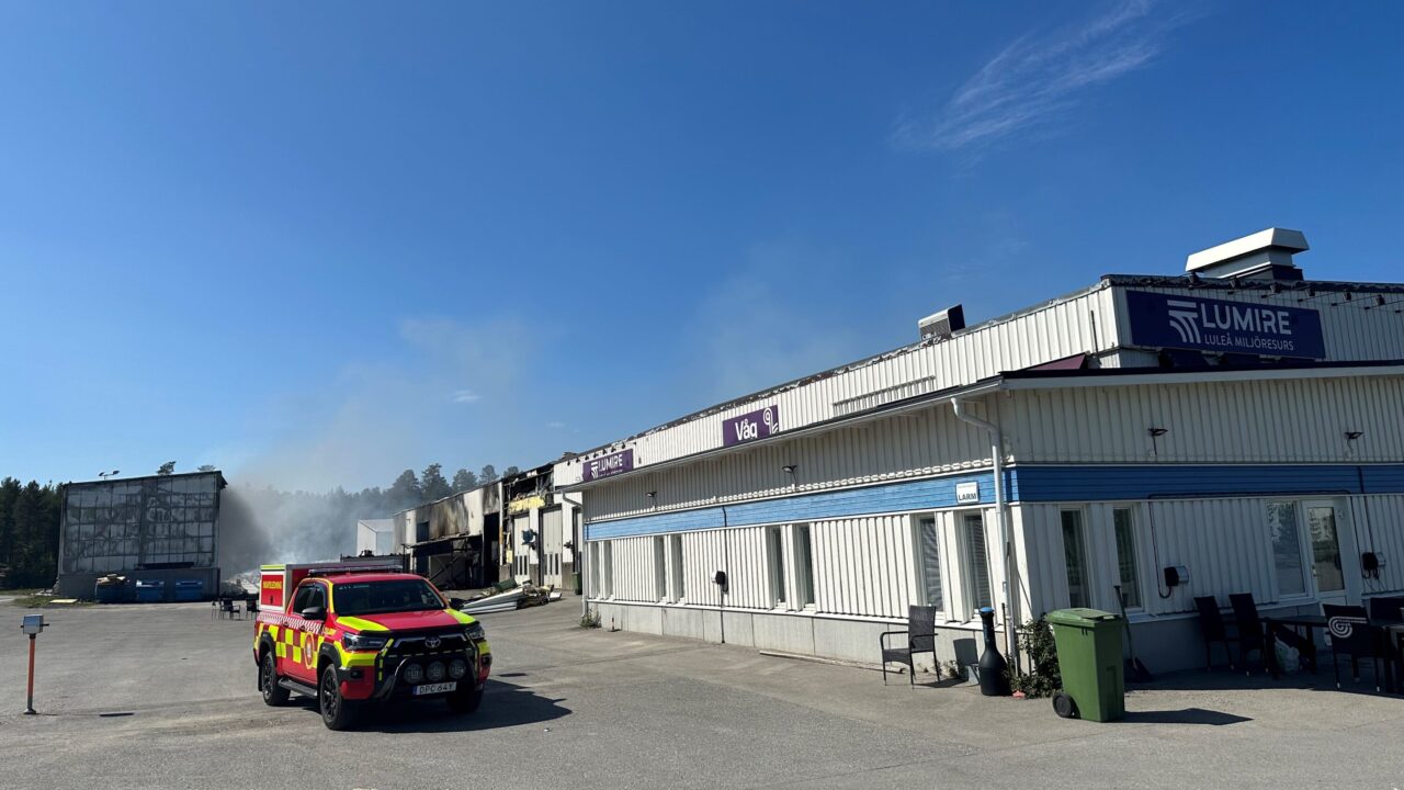 Bild på industribyggnad med räddningsfordon vid sidan av mot en blå himmel