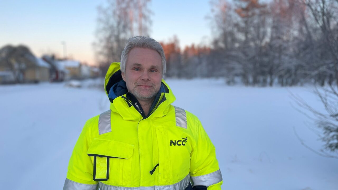 Bild på människa i gula arbets och skyddskläder utomhus i klart vinterväder med snö och sol