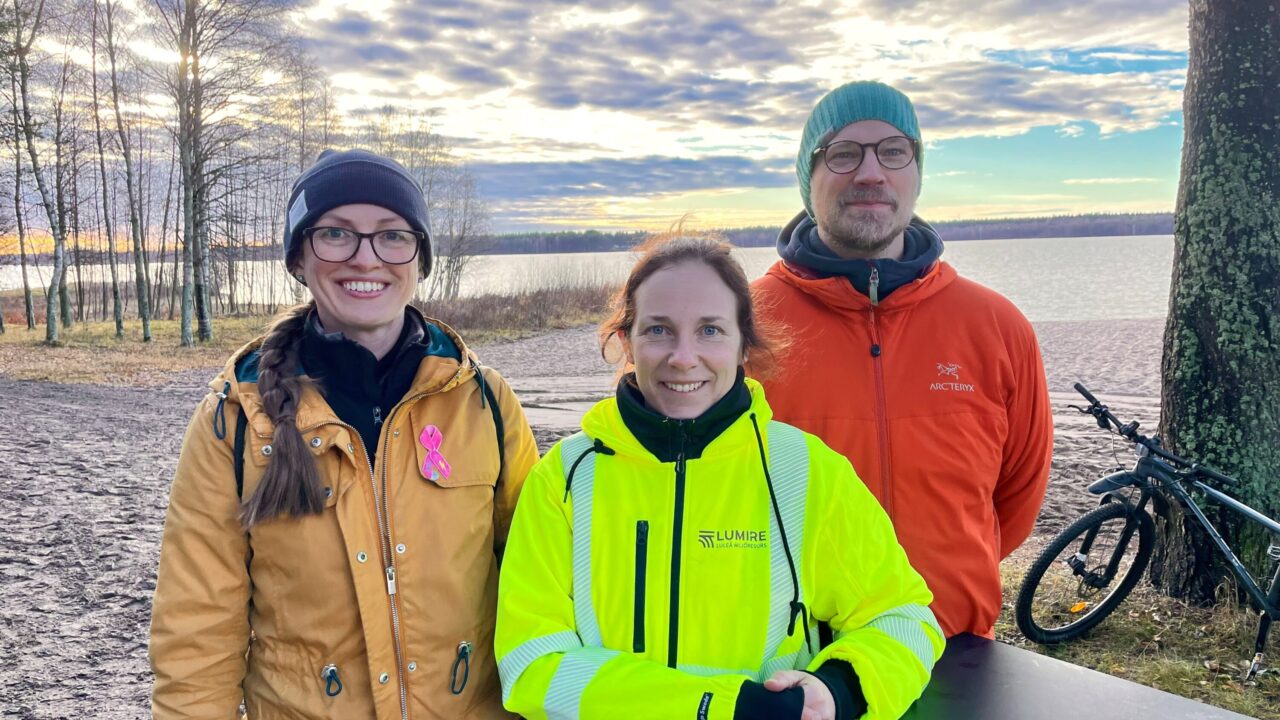 Bild på tre människor utomhus vid vatten en disig solig höstdag