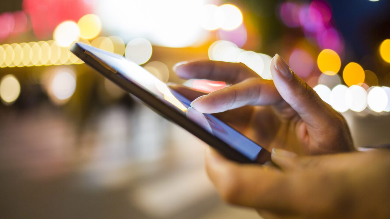 bild på hand som hålelr i mobiltelefon med ljusglimrande bakgrund
