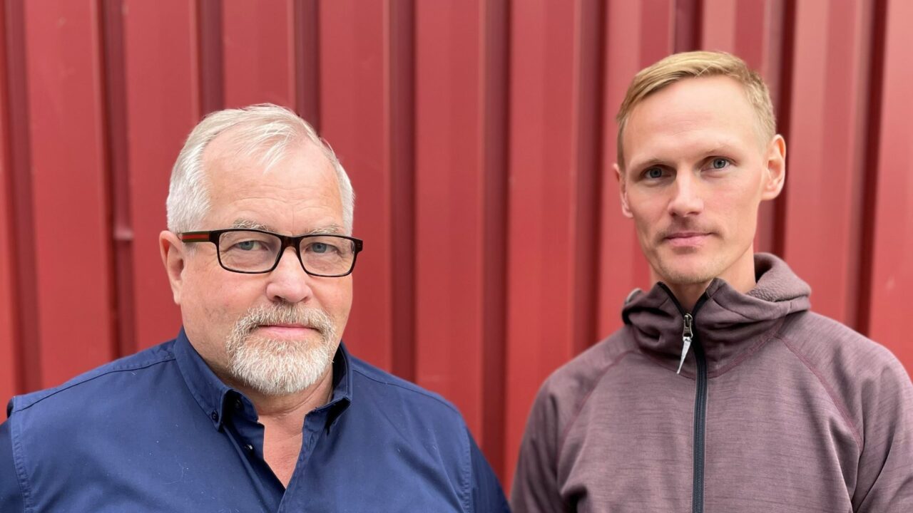 två människor står utomhus vid en röd vägg